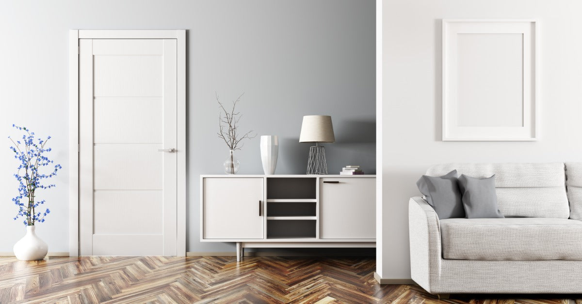  A living room in a home with a white four-panel interior door. A small, blue potted plant is right next to the doorway.