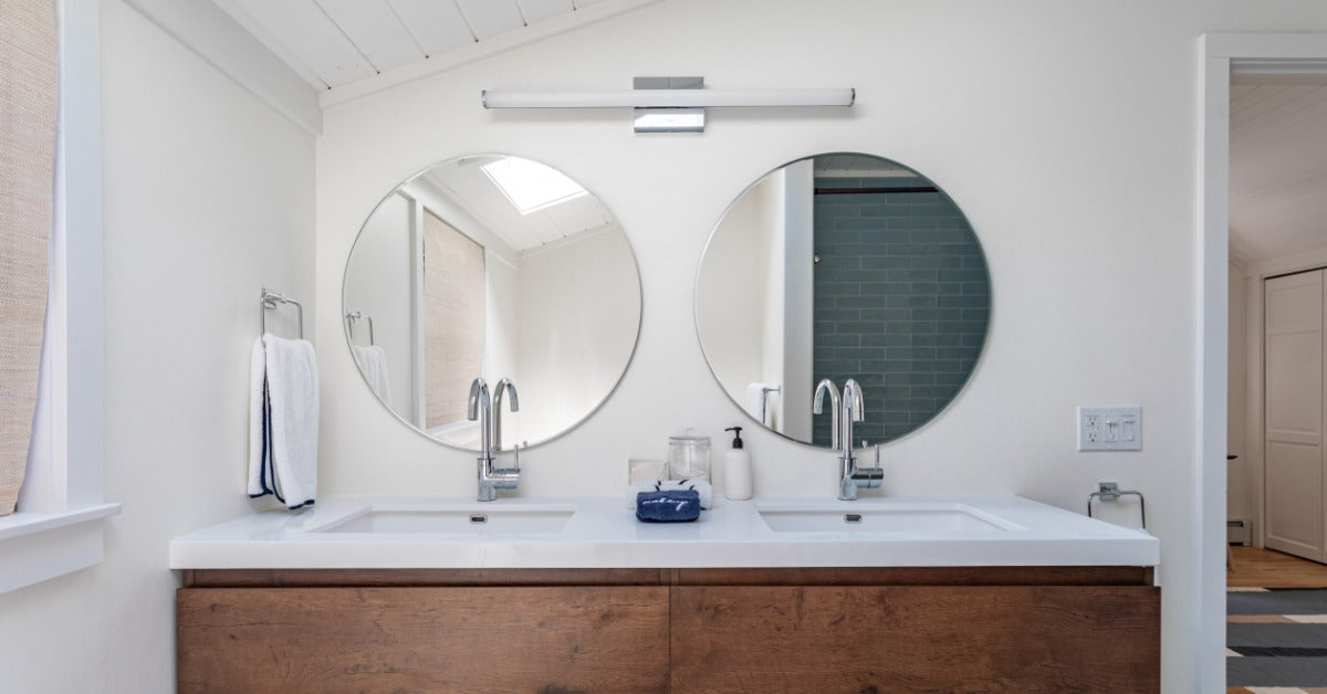A wooden double sink vanity in a residential bathroom with a white wall. Two round mirrors are installed on the wall.