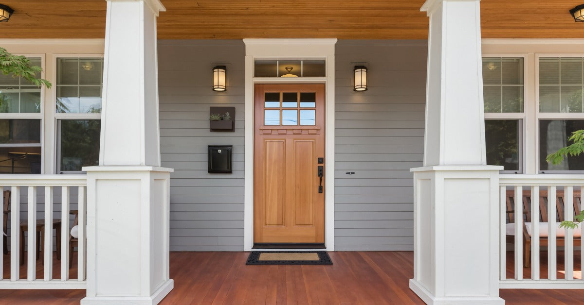 A single residential front door made of wood attached to a home with a large porch on a sunny day.