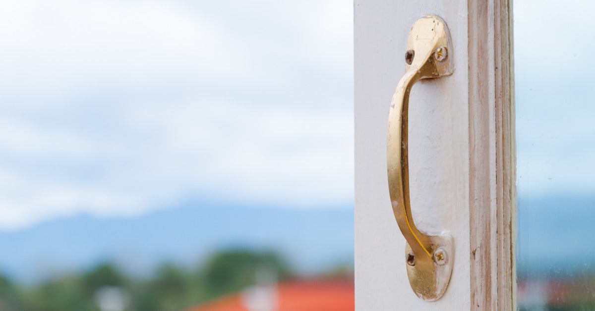 A white exterior door on a home. The gold metal handle is slightly covered in dry white paint from the door.