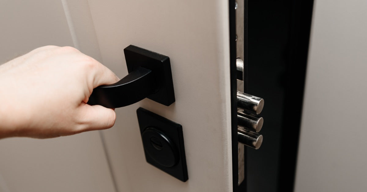 A person opening a gray door inside a home. The interior door has a long, black handle and a black lock.