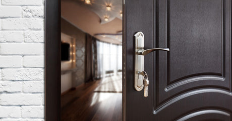 A solid wooden door with a silver metal handle open inside a home. A set of keys hangs out of the open door.