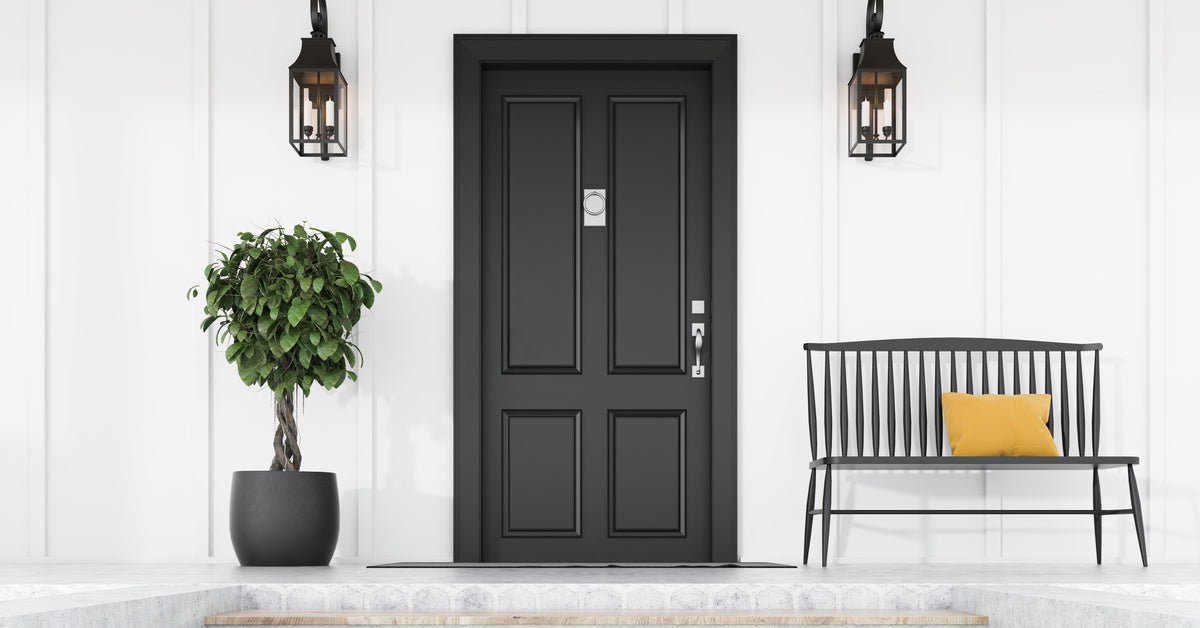A white home with a new black front door. A large potted plant and a black bench are next to the doorway.