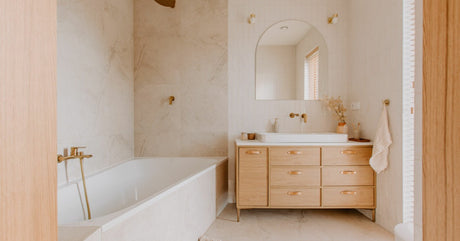 A bright residential bathroom with clean marble walls and a wooden vanity installed near the bathtub.