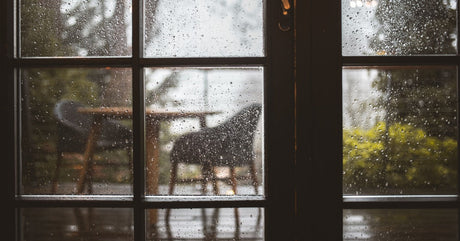 A double-door glass entryway leading to a backyard patio. Rain covers the patio and furniture outside.
